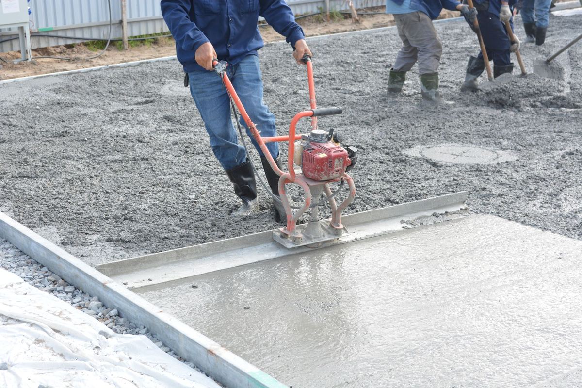 Crew screeding fresh concrete with a power screed